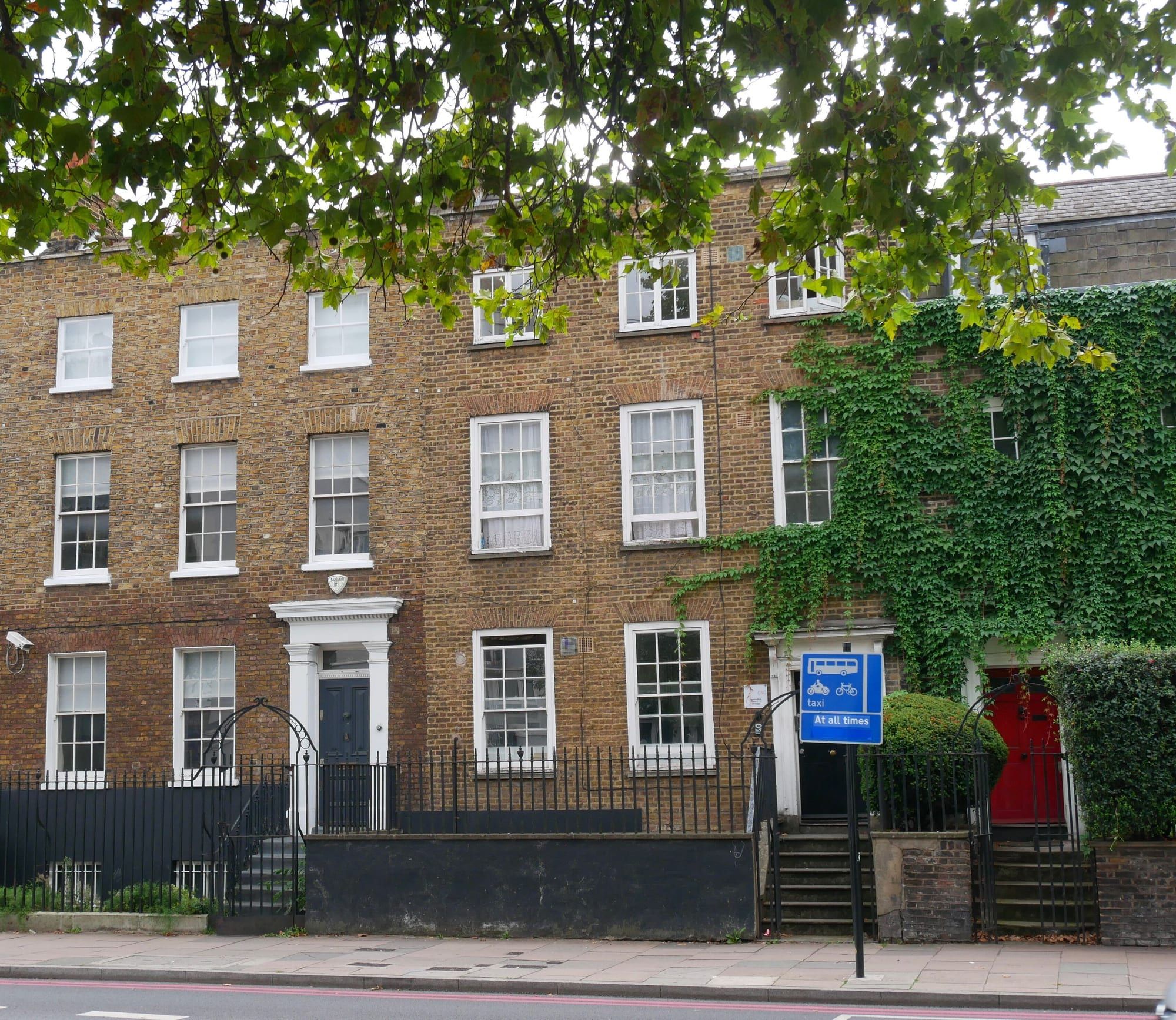 A Georgian brick terrace, partly covered in ivy, behind railings on a main road